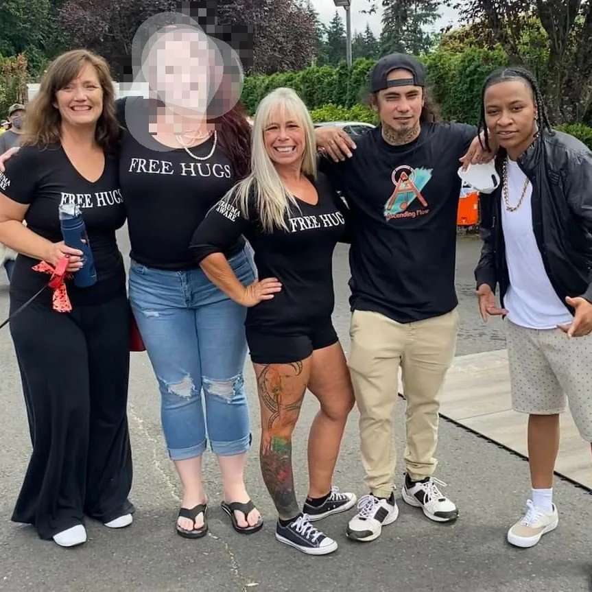 Angel Prater with four community members outdoors, wearing FREE HUGS and Ascending Flow shirts