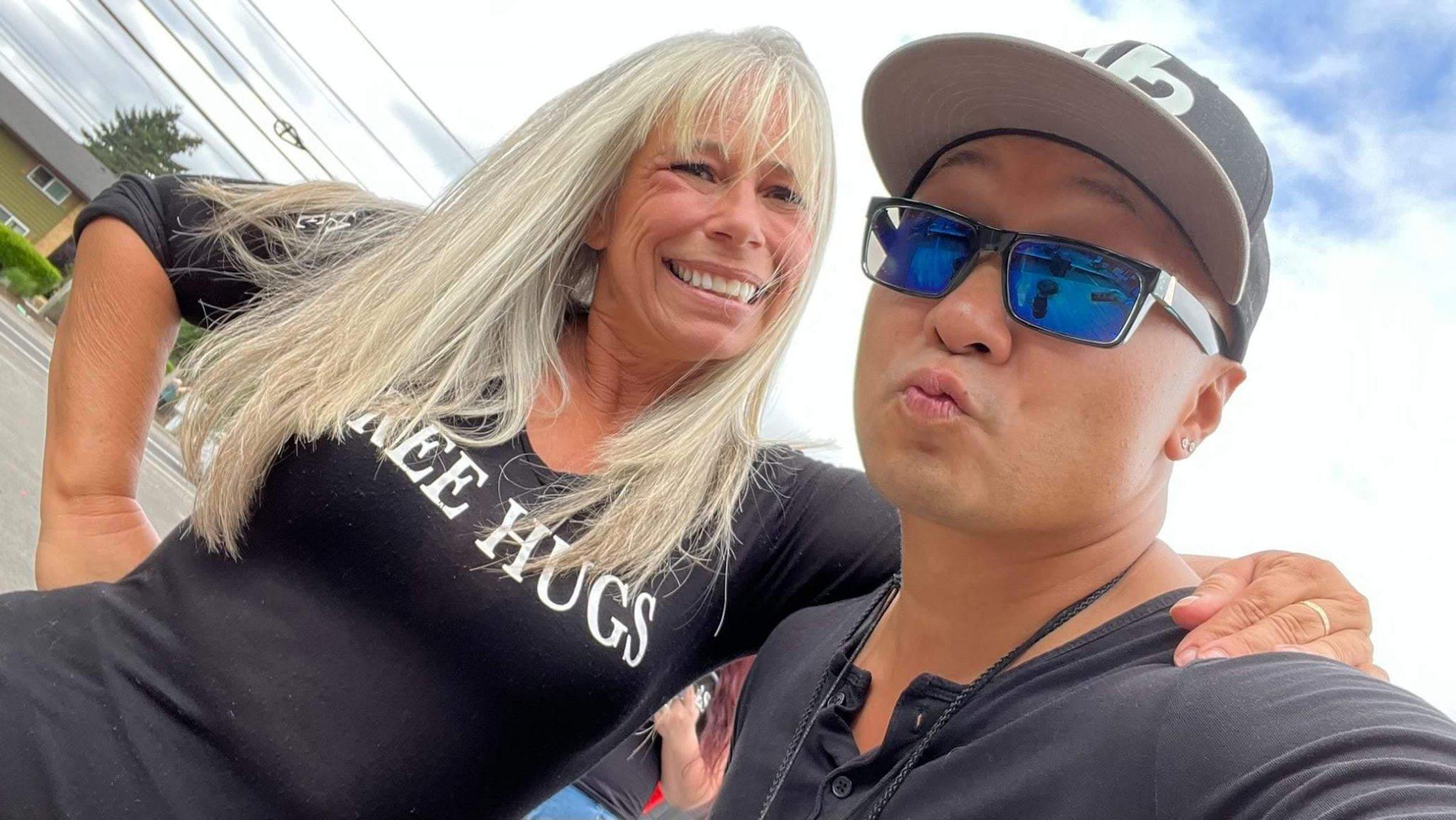 Angel Prater in a FREE HUGS shirt smiling with a member of the Ascending Flow crew in a cap and blue sunglasses