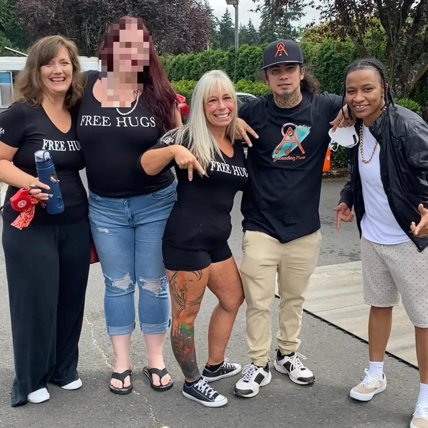 Angel Prater with four community members outdoors, wearing FREE HUGS and Ascending Flow shirts