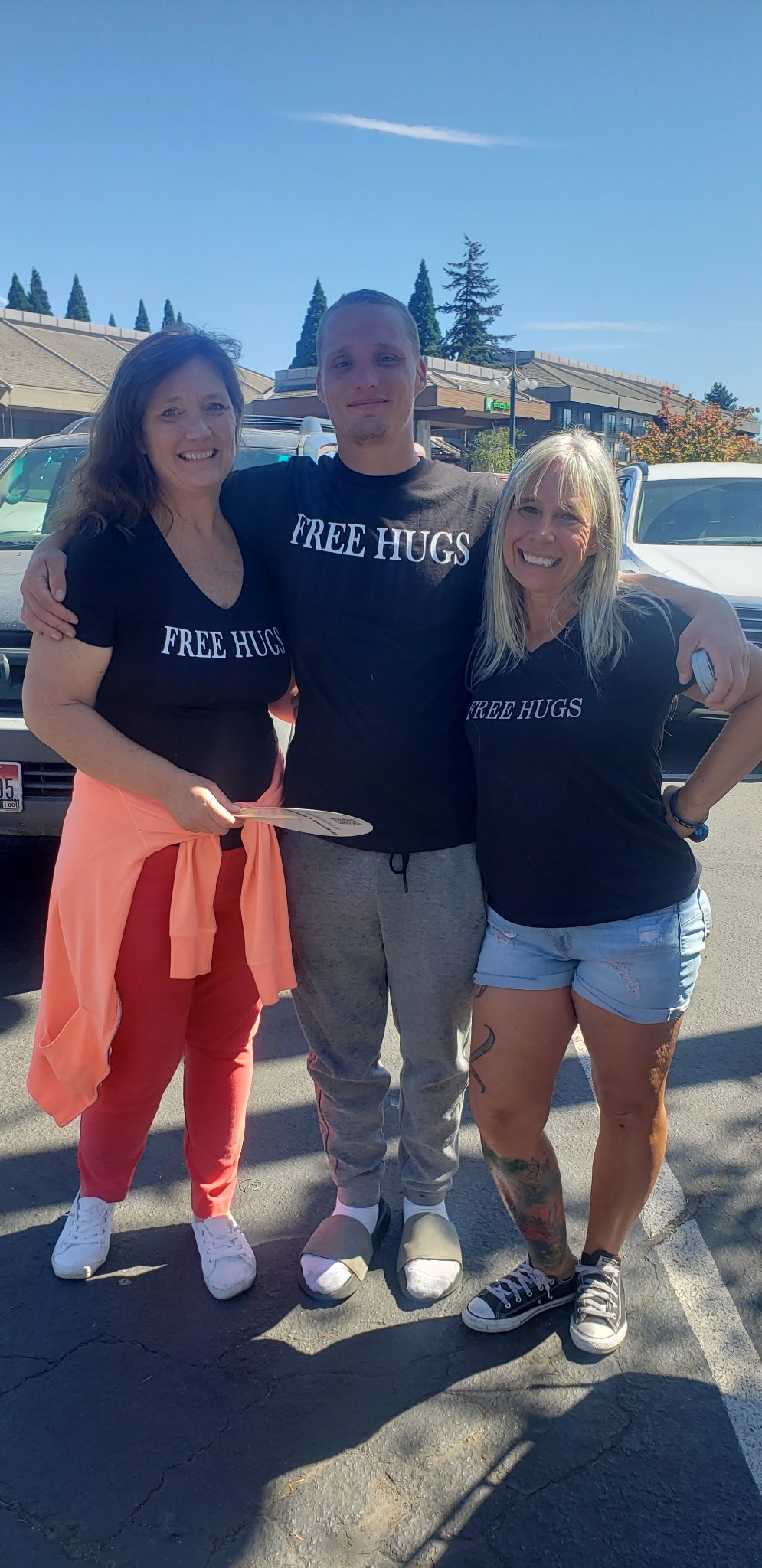 Angel Prater with two fellow crew members in a parking lot, all wearing FREE HUGS shirts