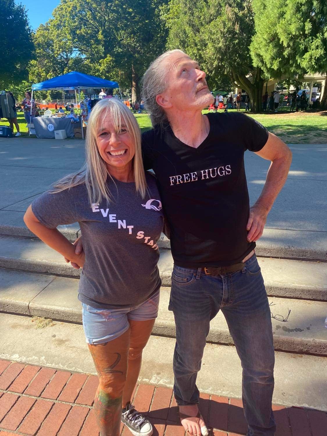 Angel Prater in an Event Staff shirt with a fellow crew member in a FREE HUGS shirt at a park event