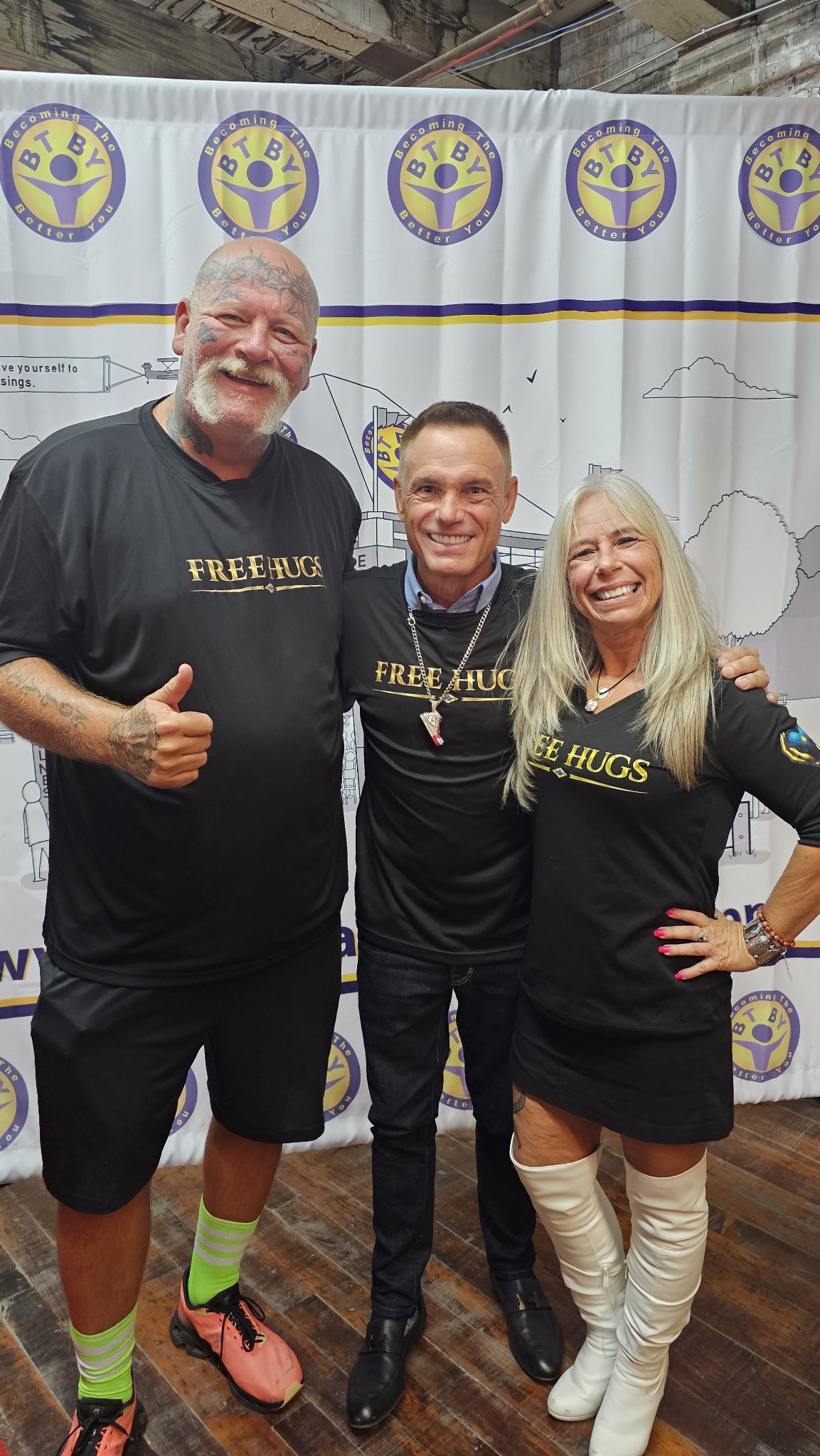 John Drury, Kevin Harrington, and Angel Prater in FREE HUGS shirts in front of a Becoming The Better You backdrop