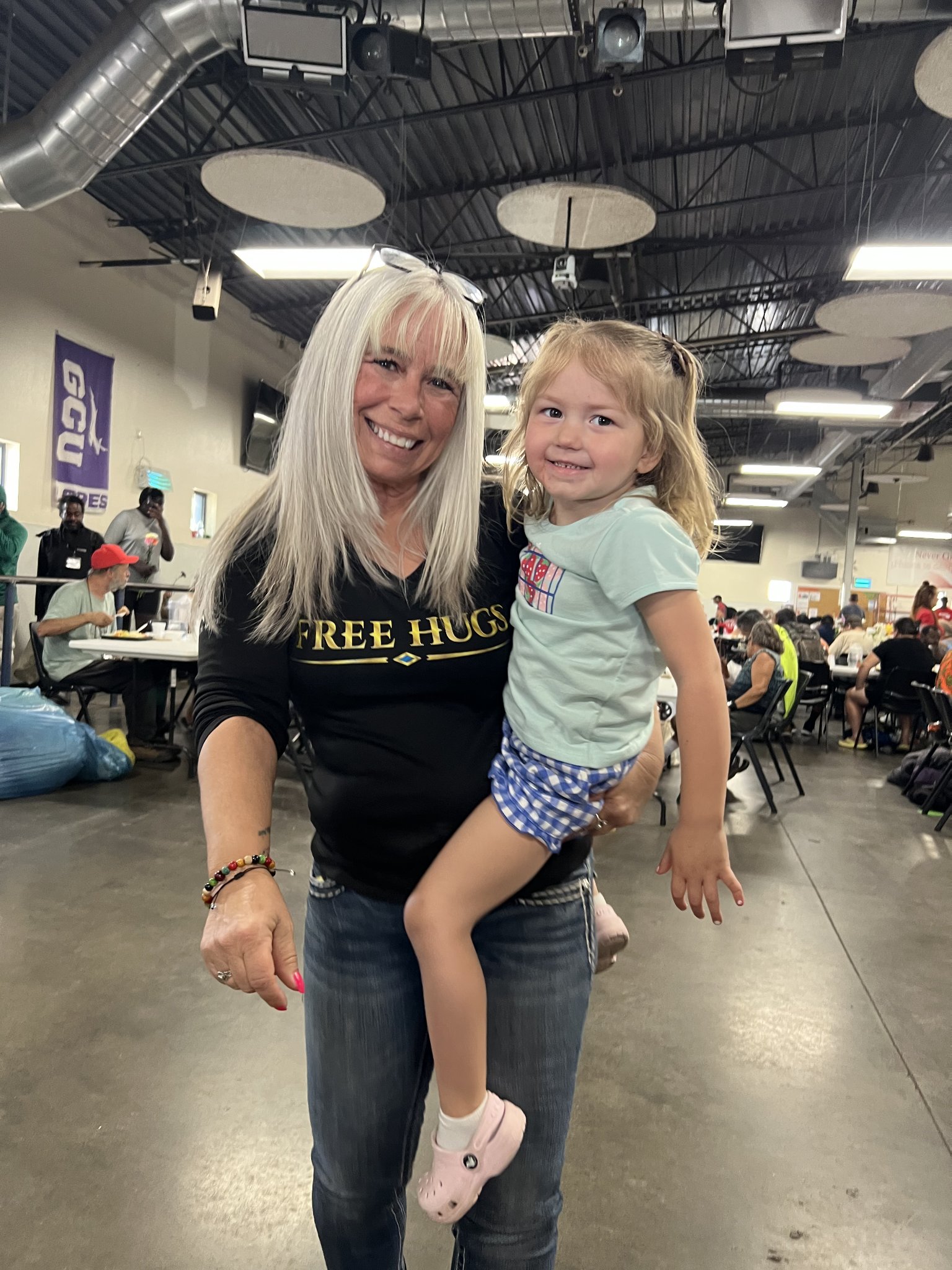Angel Prater in a FREE HUGS shirt holding her smiling 3-year-old granddaughter at a Champions for the Homeless event