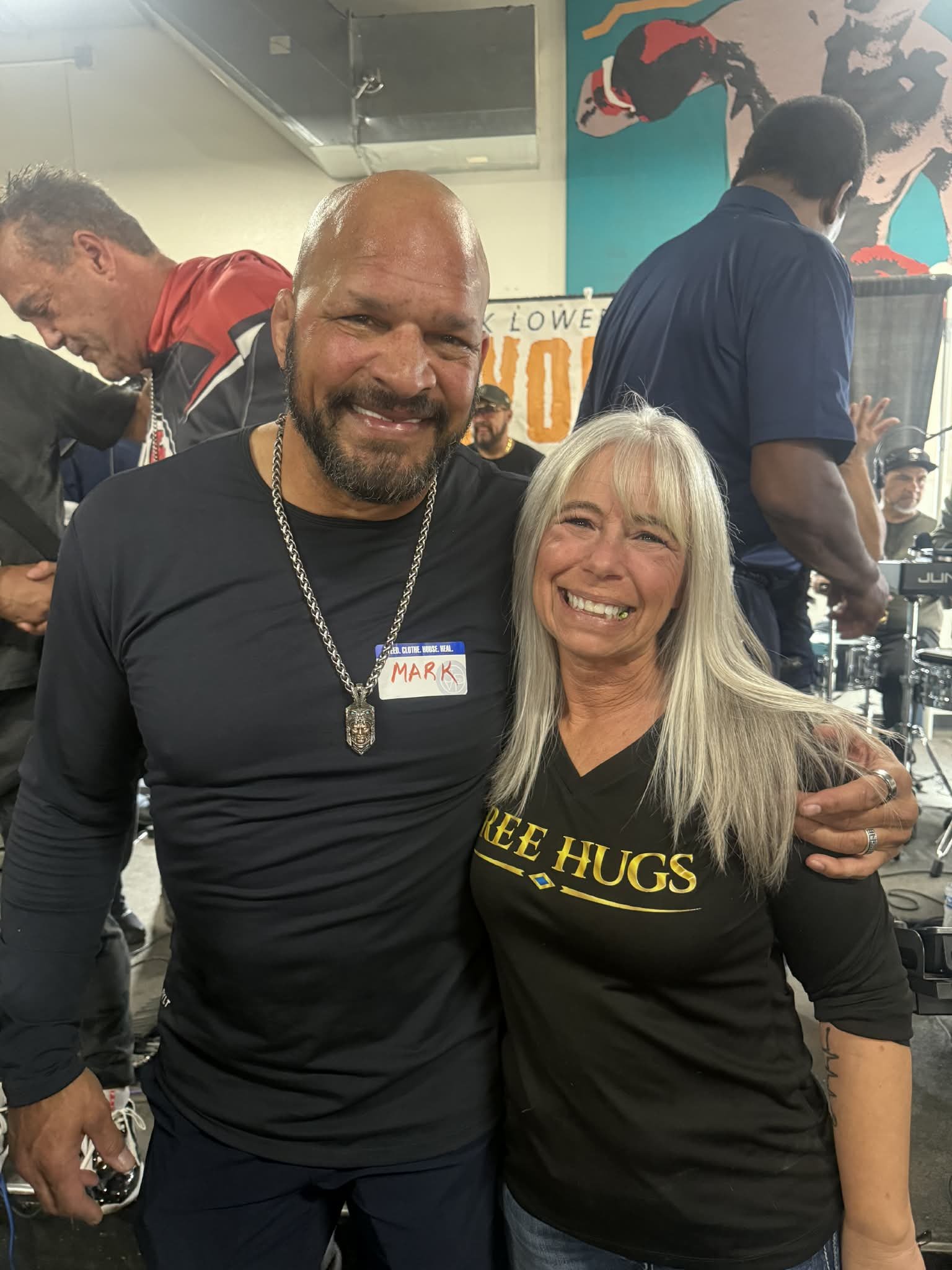 Angel Prater in a FREE HUGS shirt with Mark Kerr, wearing a handwritten MARK name tag, at a Champions for the Homeless event