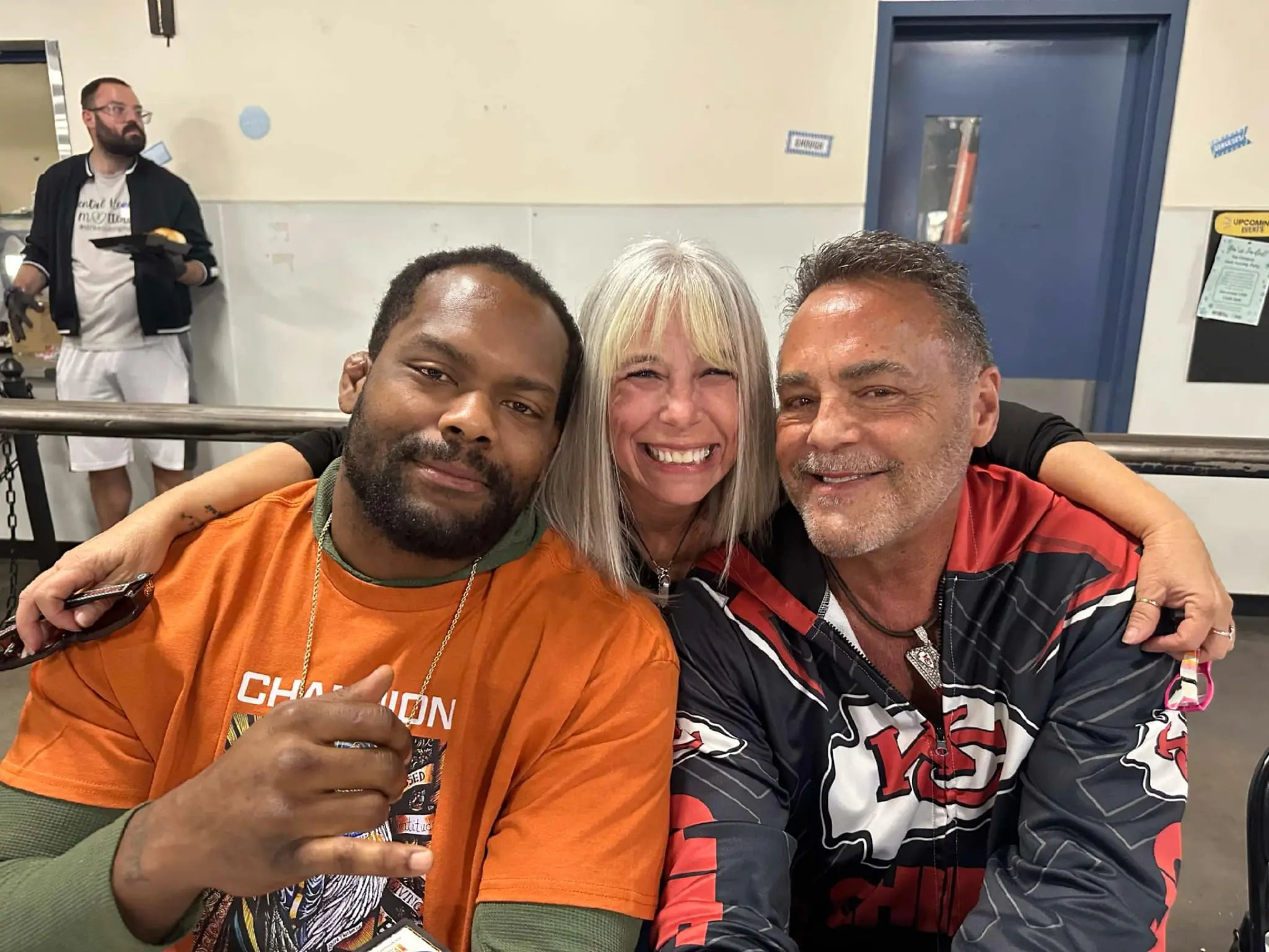 Angel Prater between a fellow guest and Nick Lowery in his Chiefs jacket in the St. Vincent de Paul dining hall