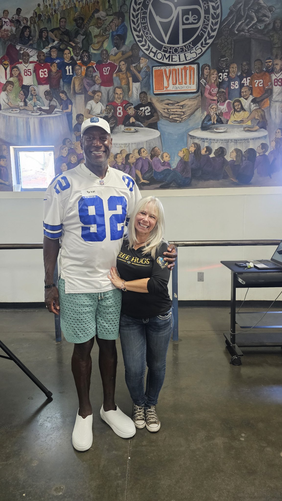 Angel Prater hugging a tall player in front of the St. Vincent de Paul Phoenix mural