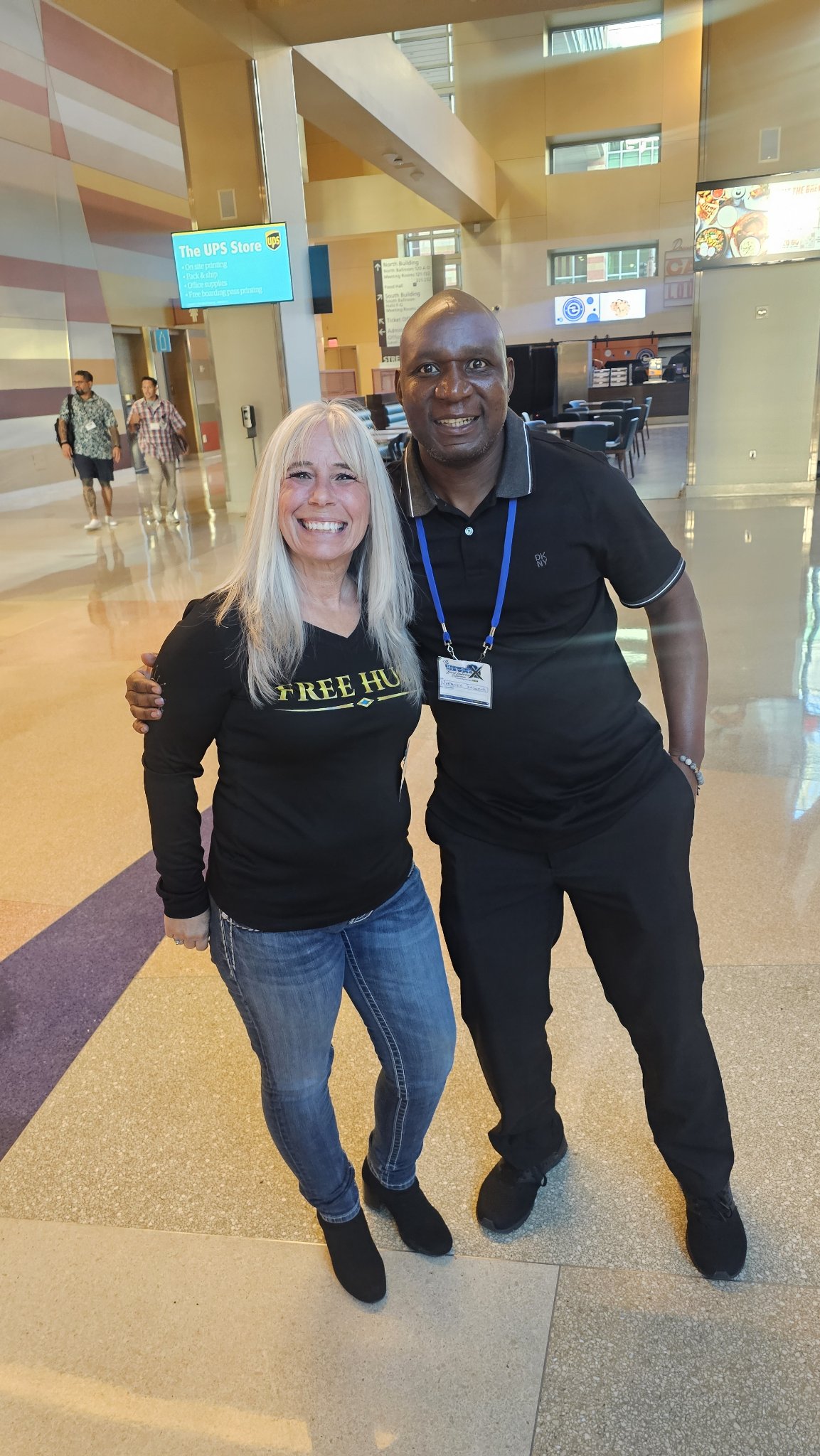 Angel Prater in a FREE HUGS shirt with a fellow attendee in a convention-center lobby