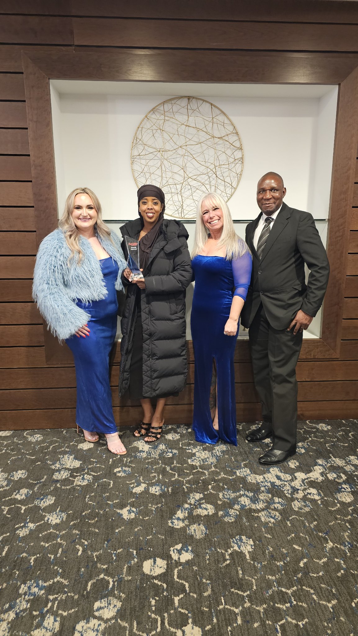 Angel Prater in a blue velvet dress with fellow guests at a gala, one guest holding an award