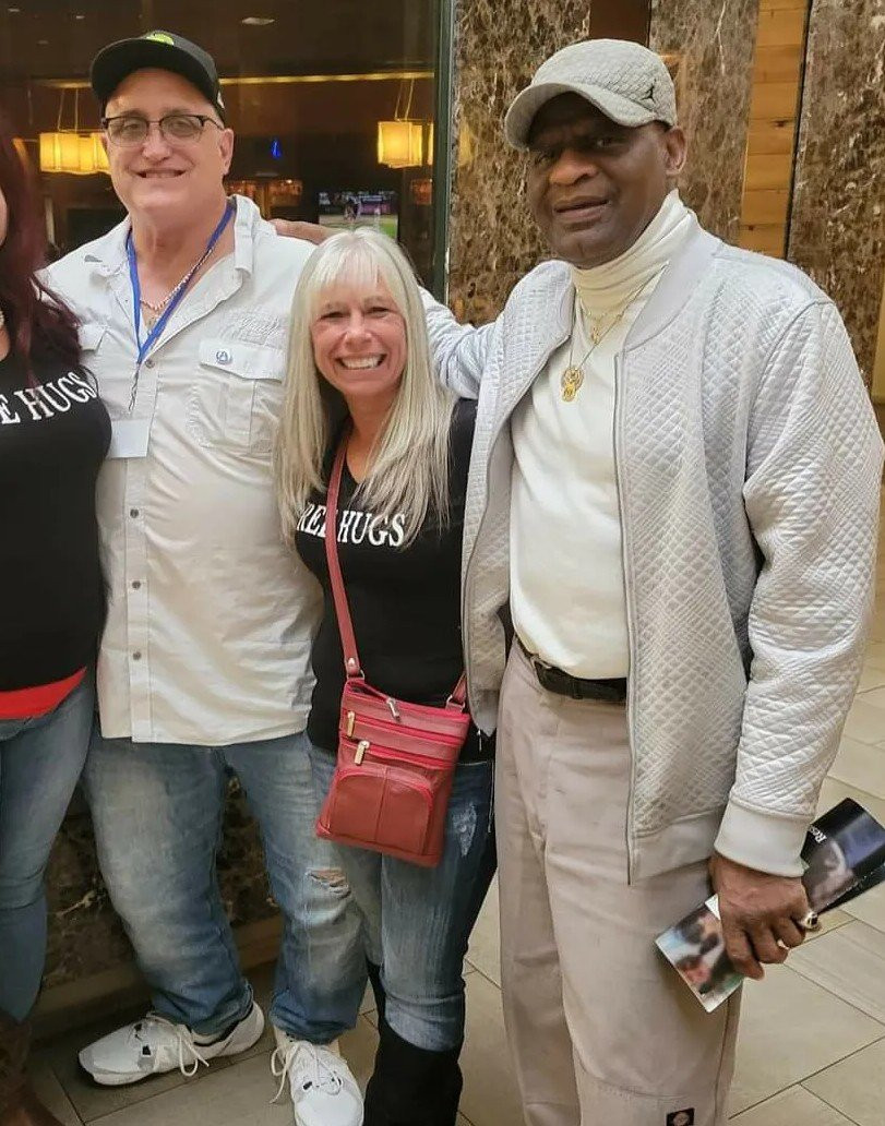 Angel Prater in a FREE HUGS shirt between two fellow conference attendees in a hotel lobby