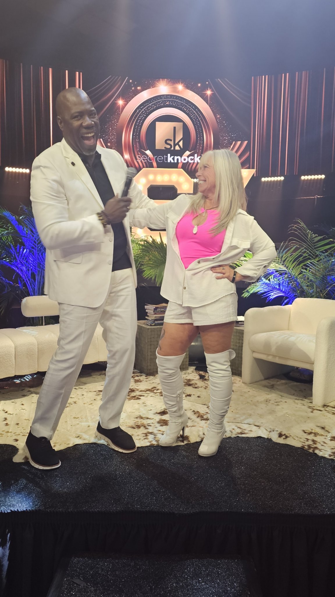 Angel Prater on the Secret Knock stage, laughing and holding a microphone toward a fellow guest