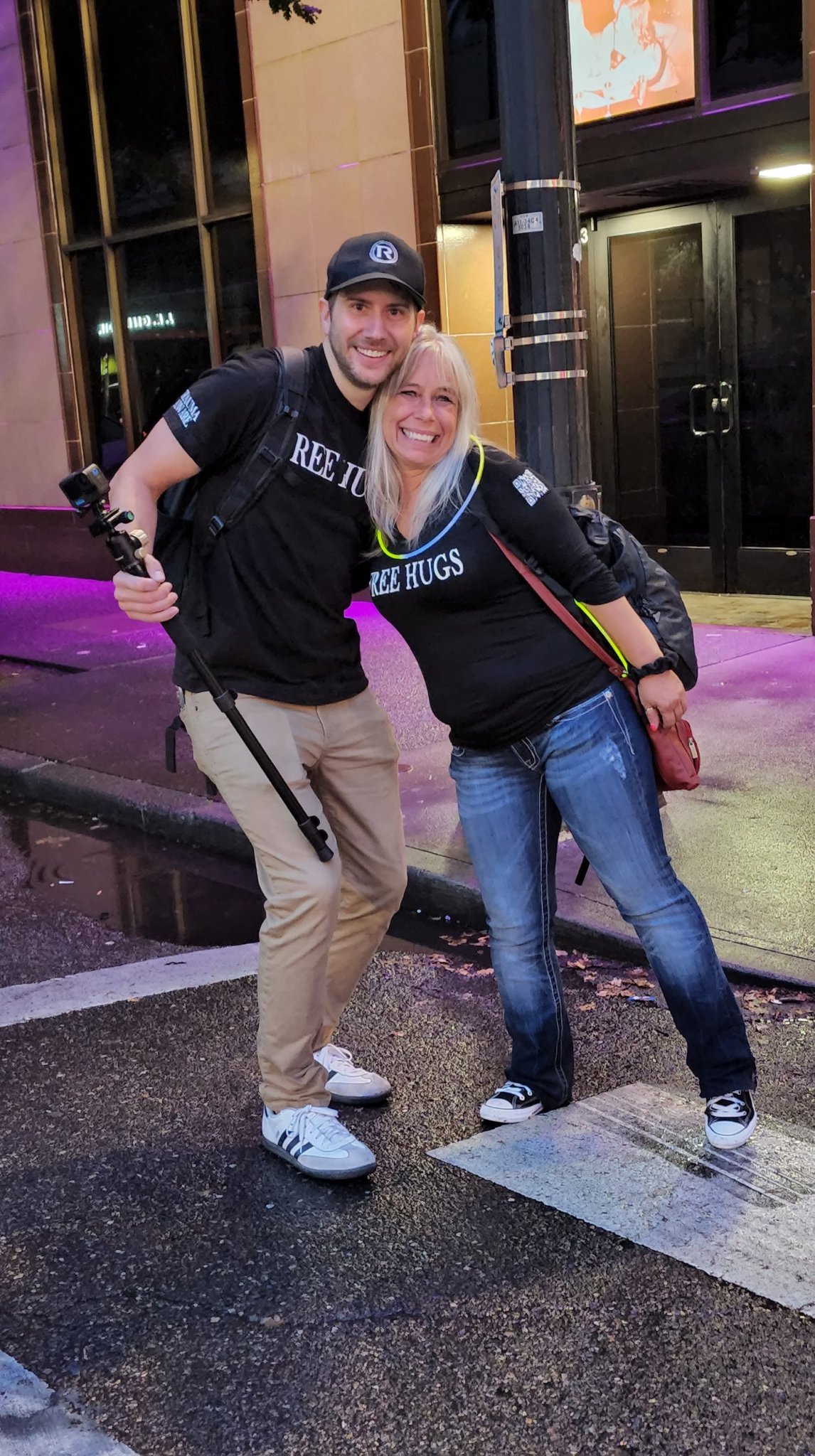 Angel Prater leaning on a fellow Free Hugs crew member holding a camera stick, on a night street at the CareOregon Starlight Parade