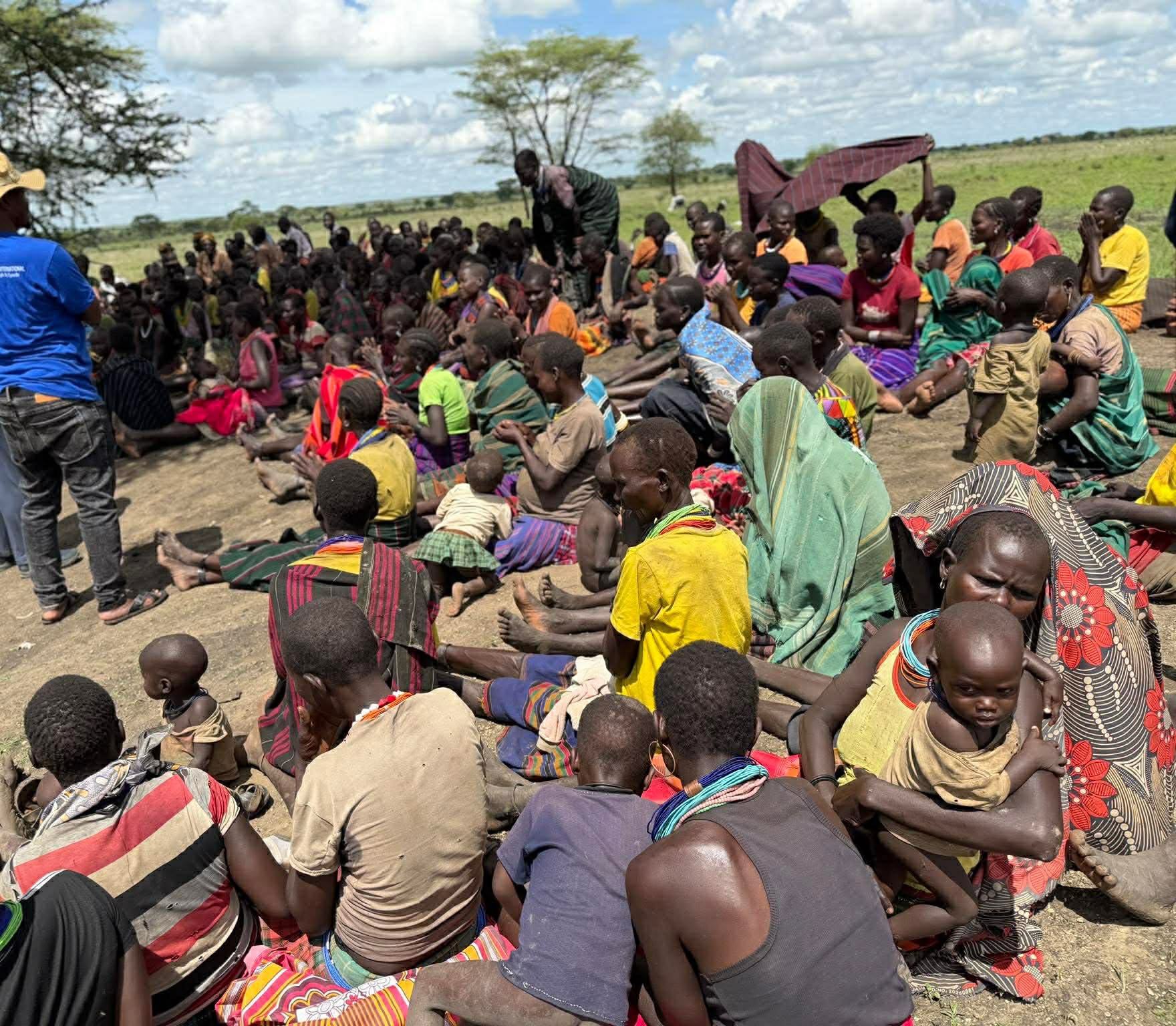 A large seated outdoor crowd of women and children from a community in Uganda