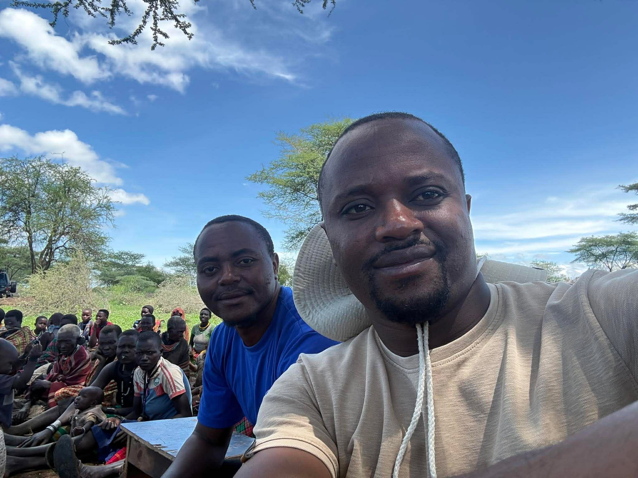 Two doctors Angel trained in Uganda taking a selfie in front of the gathered community under acacia trees