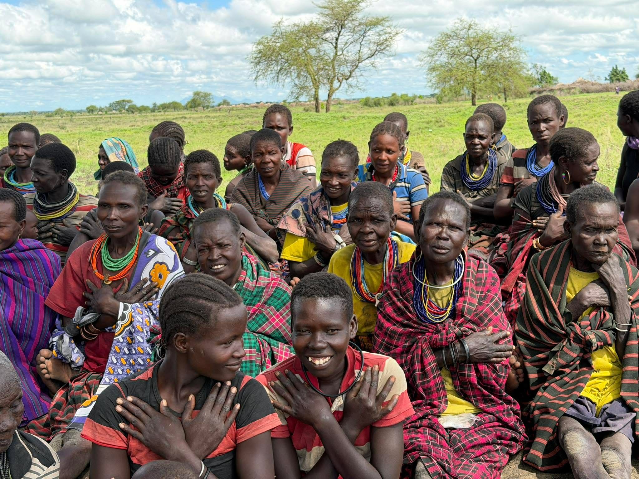 Women seated outdoors in Uganda with their hands crossed over their chests in a self-hug gesture