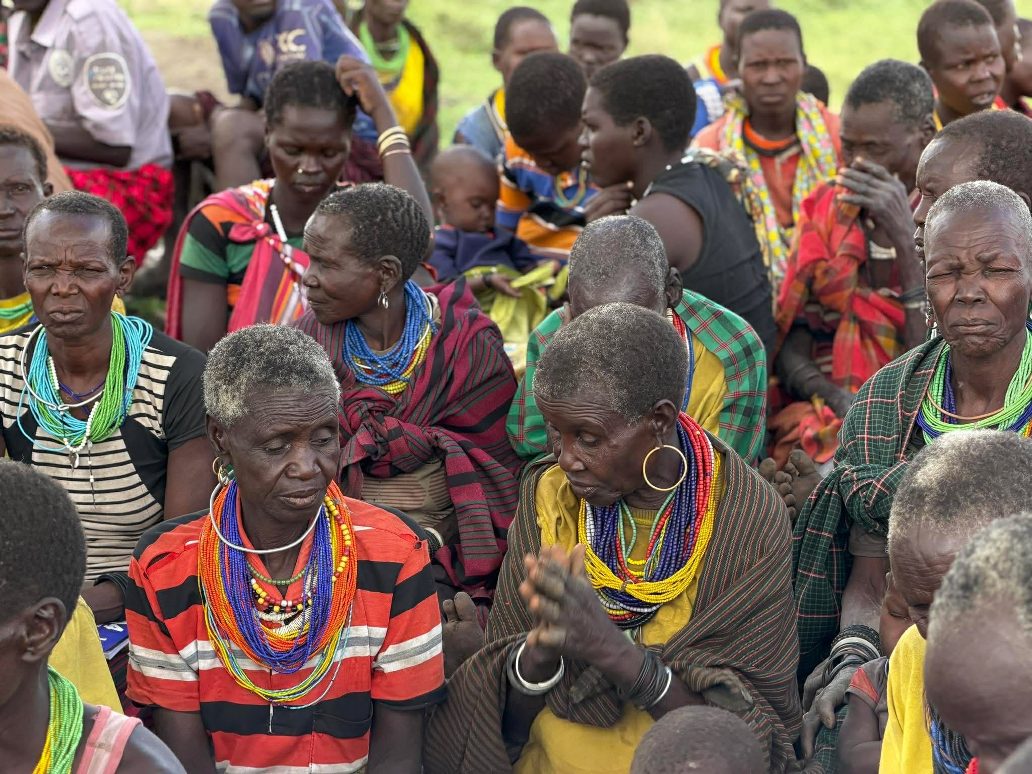 Women of a community in Uganda wearing beaded necklaces, one with her hands together