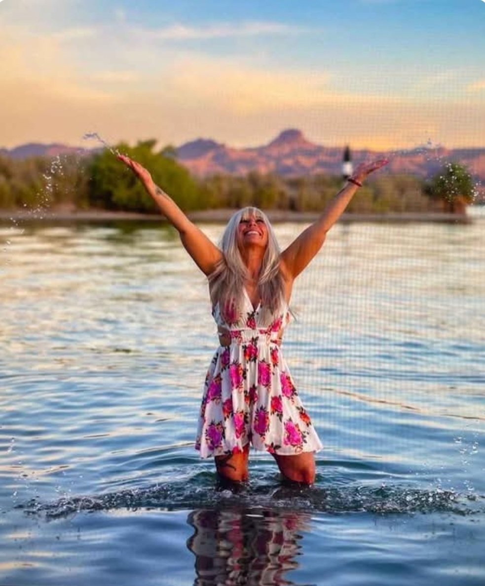 Angel Prater, CEO/Founder — standing in a lake at sunset with her arms raised