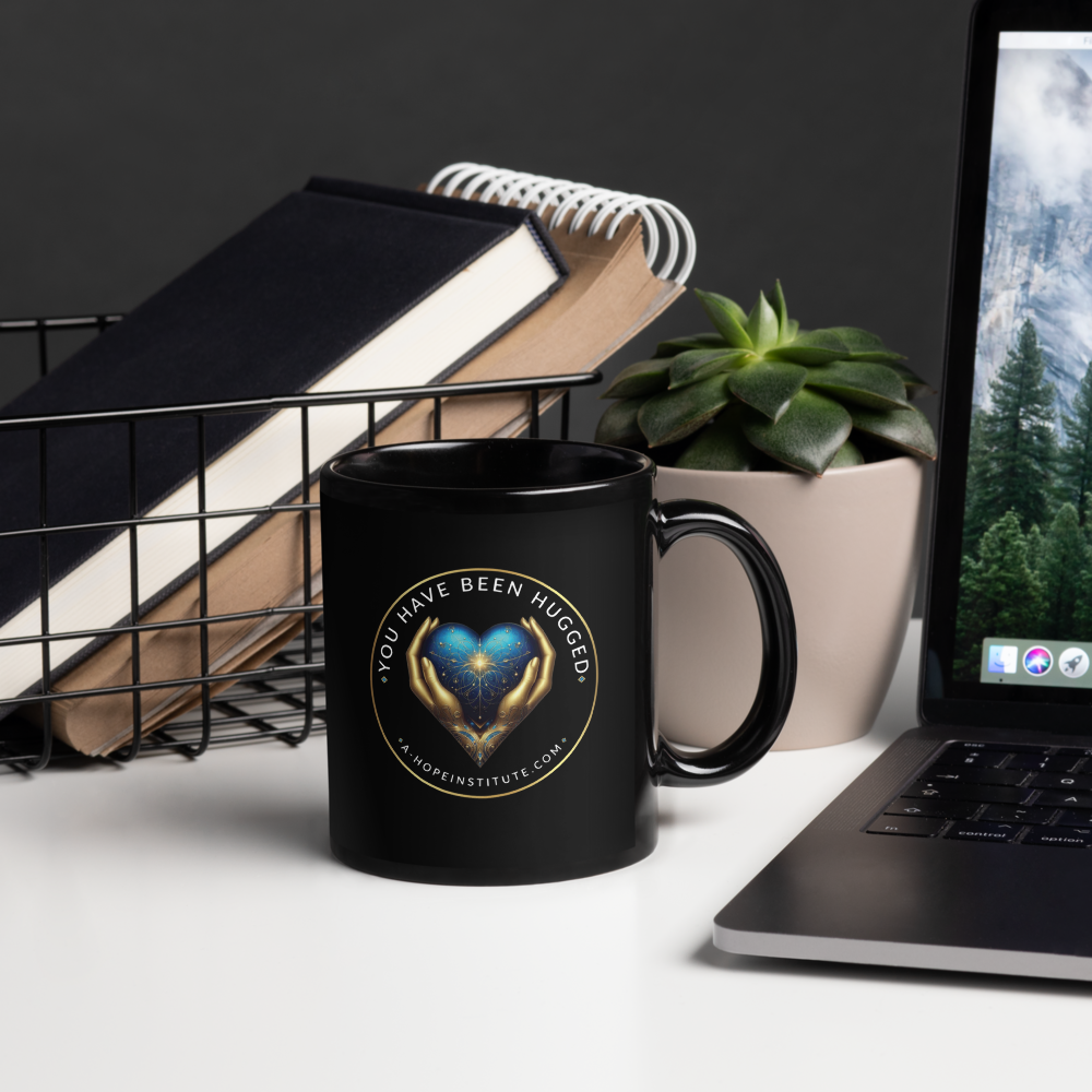 Black 'You Have Been Hugged' mug beside a laptop and notebooks